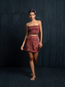 Barefoot woman wearing a red ecoprint silk strapless top and mini silk wrap skirt against a dark background.