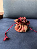 The Rimmba | Sustainable Clothing Jewelry Pouch, featuring red and beige satin tones and a secure drawstring closure, rests on a blue cushioned chair.