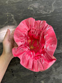 A hand holds the Rimmba | Sustainable Clothing Jewelry Pouch, crafted in pink ruffled velvet with a secure drawstring closure, displaying a gold necklace and pendant against a weathered wooden surface.