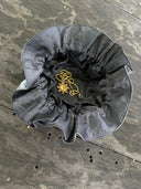 The Rimmba | Sustainable Clothing Jewelry Pouch, made of black satin with a ruffled opening and secure drawstring, sits open on a wooden surface, displaying a gold necklace with a pink and gold circular pendant inside.