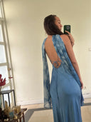 A woman takes a mirror selfie, showing her back in the Rimmba Lily Silk Dress - Aquamarine Indigo with tie-dye accents and thin ties, standing in a softly lit room decorated with candles and ornaments.