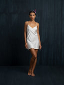 Barefoot woman wearing Mulberry silk mini dress white with thin straps. Hancrafted botanical-dyed mini dress sustainable luxury fashion for bridal and resort wear.