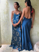 Two women stand indoors in indigo Mila Halter Silk Dresses by Rimmba | Sustainable Clothing. One faces forward; the other shows the dress's low back and a red ribbon woven into her braid.