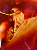 A close-up of the Mila Halter Silk Dress - Marigold from Rimmba | Sustainable Clothing, featuring marigold yellow silk fabric soaked in vibrant red-orange dye, with a braided yellow string resting on top.