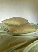Two mint green pillows from the Rimmba | Sustainable Clothing Mint Green - Full Silk Bedding Set are stacked on a matching silk sheet, set against a plain, light-colored wall.