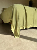 A neatly made bed features Rimmba's Mint Green - Full Silk Bedding Set, hand-dyed and bathed in warm sunlight, casting soft shadows on a beige tiled floor in a simple, cozy room.