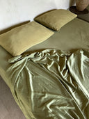 A neatly made bed with two green pillows and a slightly rumpled top sheet, all part of the Mint Green - Full Silk Bedding Set by Rimmba | Sustainable Clothing. The minimalist scene features neutral walls and a small corner table.