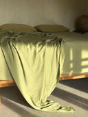 A neatly made bed features the Mint Green - Full Silk Bedding Set by Rimmba | Sustainable Clothing, with matching pillows and a silky botanical silk blanket, all in soothing mint green as sunlight casts gentle shadows across the scene.