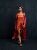 A woman wearing mini silk slip dress ecoprint red and 7/8  silk kimono ecoprint red as an outer against a dark background.