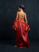 A woman facing a dark background wearing mini silk slip dress ecoprint red and 7/8 silk kimono ecoprint red. Bun hairstyle with beautiful purple orchid.