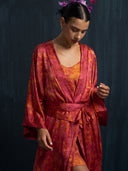 Close-up woman wearing Rimmba's Wabisabi silk kimono ecoprint red with silk belt and mini silk slip dress ecoprint red against a dark background.