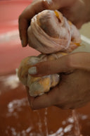 During a natural dye workshop in Bali, a person is holding pure silk, folded for eco-print process, excess water and color droplets are falling from the natural fabric on the dye bath below.