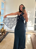 A woman stands indoors taking a mirror selfie, wearing a dark blue dress and holding out the Night Shibori - Indigo Silk Chiffon Scarf by Rimmba | Sustainable Clothing. Sunlight streams in, and candles sit on a nearby table.