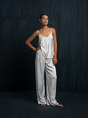 Woman wearing a white silk long pants and white camisole against a dark background.