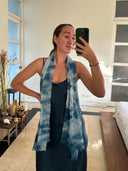 A woman in a dark blue dress and the Ocean & Waves - Indigo silk scarf by Rimmba | Sustainable Clothing takes a selfie in a bright room with a bed, candles, plants, and a large mirror in the background.
