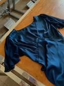The Olivia Vintage Silk Dress - Indigo by Rimmba | Sustainable Clothing, made from dark blue mulberry silk with short flutter sleeves, is displayed on a wooden table with a metal chair partly visible in the background.