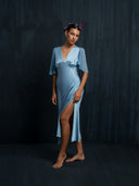 A woman wearing Mulberry Silk midi dress baby indigo with slit on the left side, v-neck style and silkchiffon sleeves against a dark background.