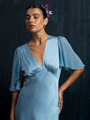 Close up woman wearing flowing Mulberry silk dress v-neck style and silkchiffon sleeves against a dark background.