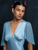 Close up view of woman wearing Mulberry silk Olivia vintage silk dress baby indigo. Hairbun style with purple flower against a dark background.