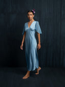 Barefoot woman wearing flowing Mulberry silk midi dress baby indigo against a dark background. v-neck style and silkchiffon sleeves.