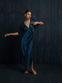 Barefoot woman wearing Rimmba's Olivia Vintage silk dress indigo V-neckline with flowing silk chiffon sleeves. She close her eyes against a dark background.
