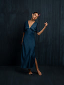 Barefoot woman closed her eyes wearing Mulberry silk dress indigo with V-neckline and flowing silkchiffon sleeves. Hancrafted botanical-dyed sustainable luxury fashion for formal and resort wear.