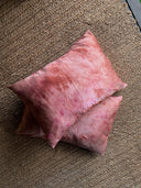 Two pinkish-brown Pua Silk Pillow Cases by Rimmba | Sustainable Clothing, hypoallergenic with a textured look, are stacked on a woven brown rug featuring a zigzag edge in the top right corner.