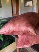 The Pua Silk Pillow Case 2x Set by Rimmba | Sustainable Clothing sits on a wooden table next to a green fern. Arched doorways, beige walls, and a round mirror with reflected plants create a serene indoor backdrop.