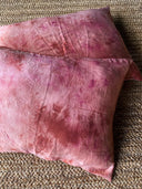 The Pua Silk Pillow Case 2x Set by Rimmba | Sustainable Clothing features pink, tie-dyed cases with subtle creases and shades, resting on a natural jute rug with hypoallergenic covers for added comfort.