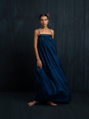 Barefoot woman wearing flowy silk maxy dress indigo with a thin straps and gathered bust detail. luxury fashion for bridal, formal , and resort wear.