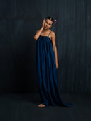 Left side view of barefoot woman wearing a maxy sillk dress indigo with thin straps and gathered bust detail. Luxury fashion for bridal, formal, and resort wear.