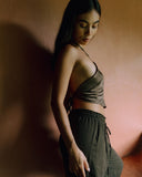 A woman standing with long black hair wearring Mulberry Silk halter top Mud-dye against a brown background.