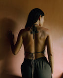 A back view of woman wearring Halter silk top and matching colour pants facing a brown wall.
