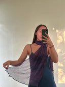 Indoors, a woman takes a mirror selfie in a dark sleeveless dress, draping the Rimmba | Sustainable Clothing "Purple Sunset" Silk Chiffon Scarf around her neck as sunlight casts patterns on the wall behind her.