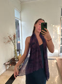 A woman takes a mirror selfie indoors, wearing a dark dress and holding out Rimmba | Sustainable Clothing's "Purple Sunset" silk chiffon scarf. The sheer, naturally dyed scarf appears purple in a sunlit room with plants and decor.