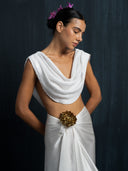 Woman wearing a white silk linen blouse cowl neckline and white silk sarong with a bronze brosche against a dark background.