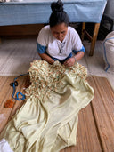 A woman sits sewing emerald Shibori patterns onto silk for the Scarlette Silk Dress by Rimmba | Sustainable Clothing, surrounded by threads and tools as she carefully crafts each detail.