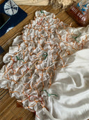 A white mulberry silk fabric, tied with orange and green strings in a grid for tie-dyeing, lies on a bamboo mat—ideal for making the Rimmba | Sustainable Clothing Scarlette Silk Dress - Emerald Shibori.