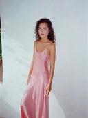 A woman with curly hair wears the Rimmba Scarlette Silk Dress - Full Length Maxi, posing calmly against a plain light wall.