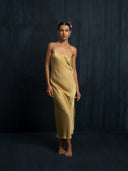 Barefoot woman wearing a luxury midi silk dress in mango colour with thin straps. Luxury fashion for bridal, formal, and resort wear.