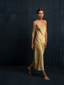 A woman wearing Rimmba's Scarlette silk midi dress mango. Luxury midi silk dress with thin straps and slit against a dark background.