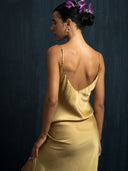 Close-up back view of woman wearing midi silk dress in mango colour with thin straps and slit against a dark background.