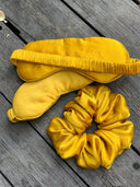The Rimmba Silk eye-mask - Solids and matching yellow silk scrunchie rest on a weathered wooden surface, offering luxury, sustainability, and anti-aging benefits for your nightly routine.