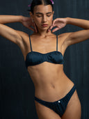 Woman wearing a silk intimate set indigo bra & underwear with a dark background.