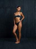 Woman wearing a silk intimate set indigo bra & underwear with a dark background.