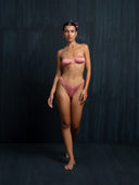 Barefoot woman waering silk intimate set in pink against a dark background.
