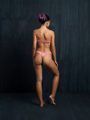 A woman facing a dark background wearing silk intimate set underwear pink.