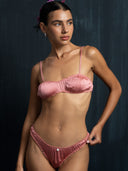 Close-up woman wearing silk intimate underwear set in pink against a dark background.
