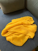 a yellow silk chiffon scraf loosely folded on a blue upholstered sofa. The sofa has a matching blue cushion in the corner, giving a cozy indoor feel.