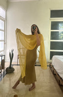 Karunia Fischer's taking a mirror selfie indoors, wearing a long, flowing yellow dress with a silkchiffon yellow scarf draped gracefully over one arm.
